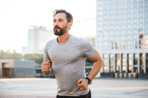 Image of handsome strong mature sportsman running at the street outdoors looking aside.