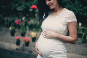 Pregnant woman in white dress holding her stomach