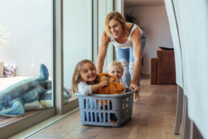 Mother playing with her children at home. Pushing them in a laundry basket.