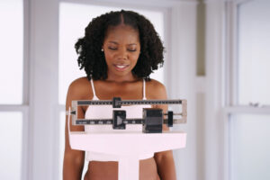 Young woman weighs herself on scale disappointed with weight gain.