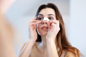 Woman adjusting her nose bandage after nose surgery while looking in the mirror.